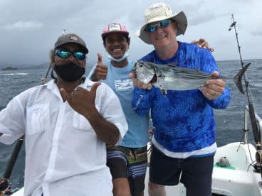 Three anglers celebrating a successful catch of a Bonito while fishing in open waters, showcasing camaraderie and excitement.