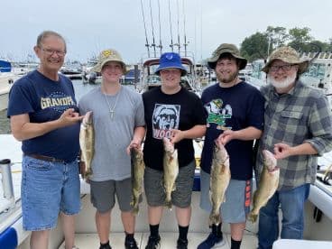 A family group proudly displaying their catch of Walleye after a successful fishing trip, showcasing a mix of ages and smiles on a boat.