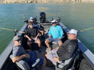 Group of anglers relaxing inside a modern fishing boat on a calm lake, showcasing comfortable seating and fishing gear.