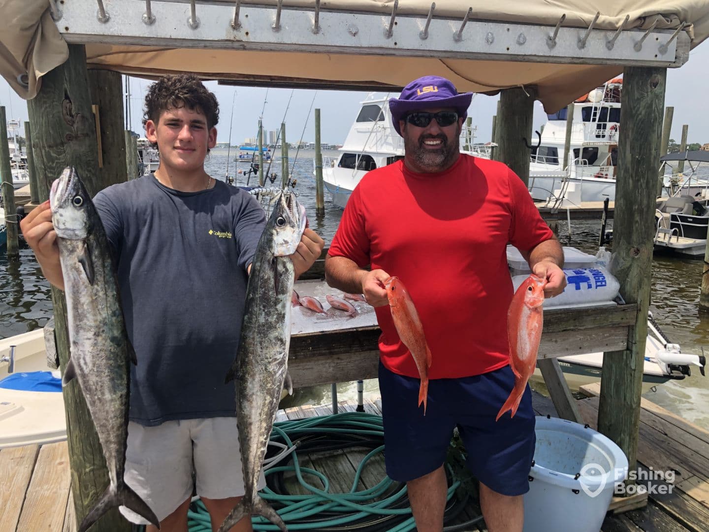 A young angler and an adult proudly displaying their catch of two King Mackerel and two Red Snapper at the dock, showcasing a successful fishing trip.