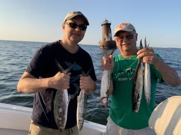 Two anglers proudly displaying their catch of Spanish Mackerel while enjoying a fishing trip on the water.