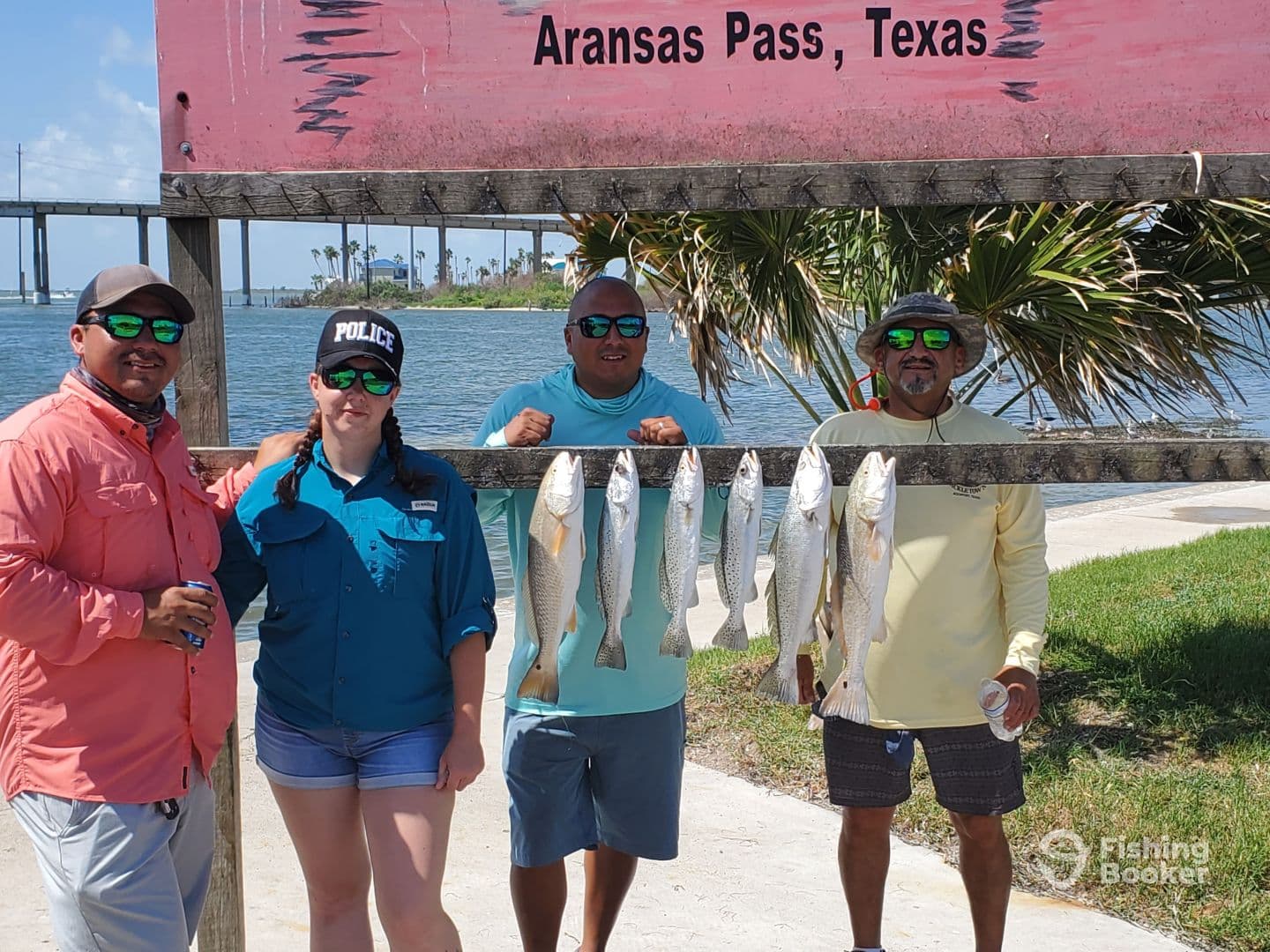 A group of four anglers proudly displaying their catch of Speckled Trout on a board in Aransas Pass, Texas, showcasing a successful fishing trip.