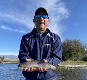 An angler proudly displaying a Rainbow Trout while fishing in a scenic river setting.