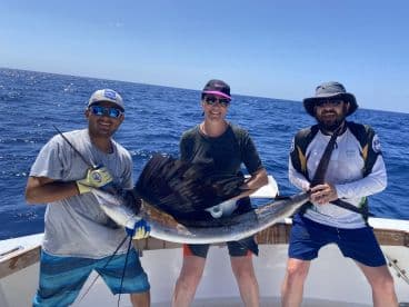 Three anglers proudly displaying a large Sailfish aboard a sport fishing boat in open waters.