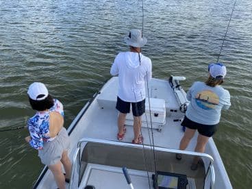 A family enjoying a fishing trip on a small boat, actively casting lines into the water in a scenic fishing environment.
