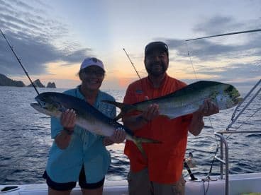 Two anglers proudly displaying their Mahi Mahi catches during a sunset fishing trip off the coast.