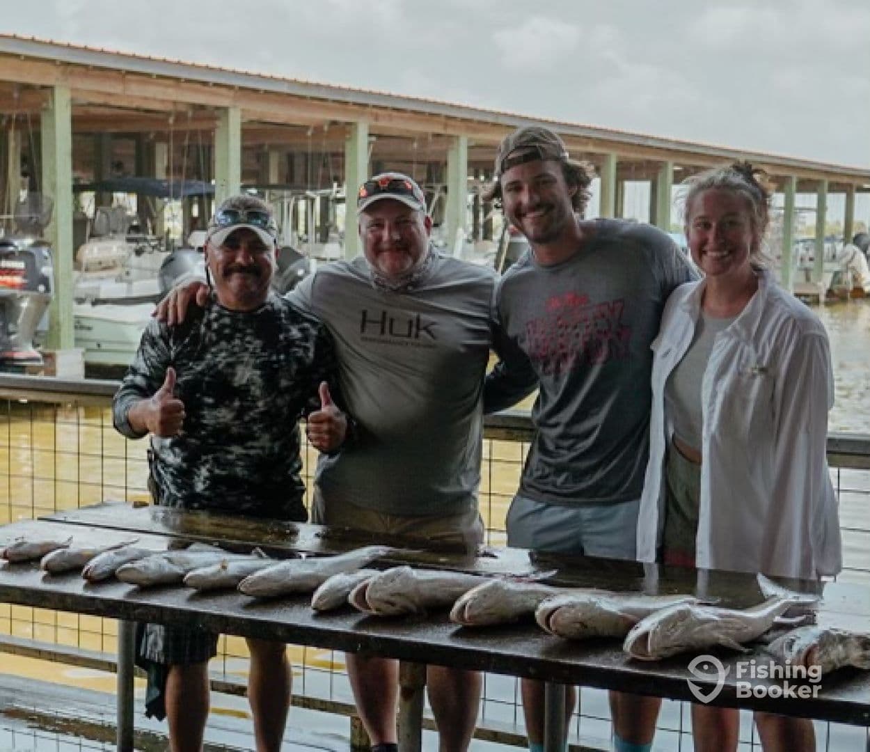 A group of four anglers proudly posing with their catch of fish displayed on a board at a marina, showcasing a successful fishing trip.