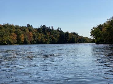 Scenic view of a calm river surrounded by colorful autumn foliage, ideal for a peaceful fishing experience.