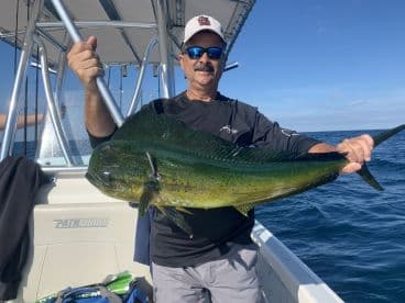 An angler proudly displaying a vibrant Mahi Mahi aboard a Pathfinder boat during a deep-sea fishing trip.