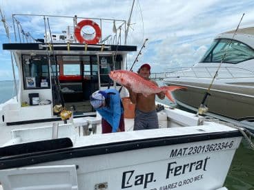 An angler proudly displays a large Red Snapper aboard a charter boat, showcasing a successful fishing trip in a coastal environment.
