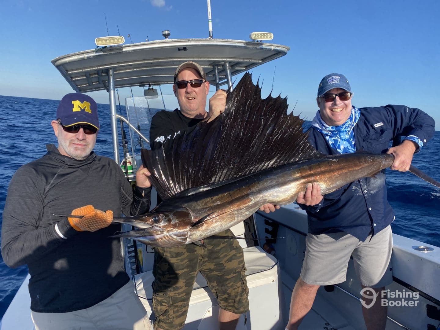 Three anglers proudly displaying a large Sailfish aboard a fishing boat in open waters.