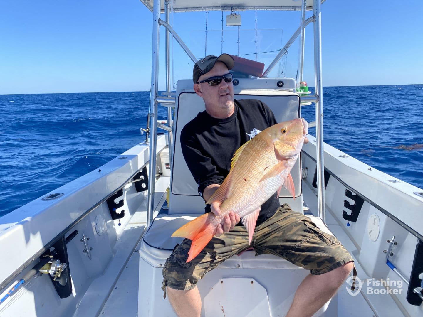 Angler holding a large Yellow Snapper aboard a fishing boat in open waters, showcasing a successful deep-sea fishing trip.