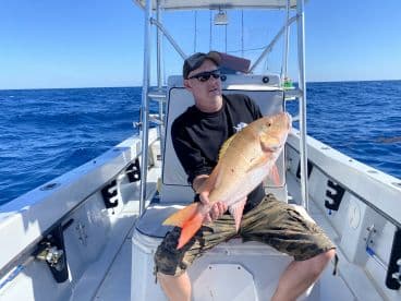 Angler holding a large Yellow Snapper aboard a fishing boat in open waters, showcasing a successful deep-sea fishing trip.