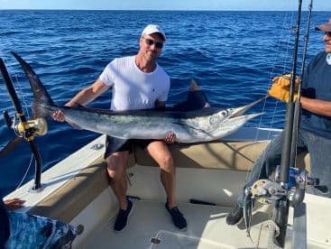 An angler proudly displaying a large Mahi Mahi aboard a sport fishing boat in open waters.