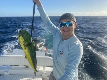 An angler proudly displaying a vibrant Mahi-Mahi while fishing offshore, showcasing a sunny day on the water.