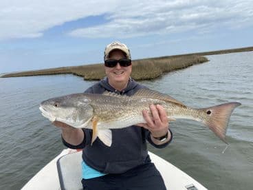 An angler proudly displaying a large Redfish while fishing in a scenic marsh environment.