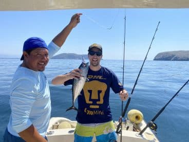 Two anglers proudly displaying a caught fish while fishing on a calm day at sea, showcasing a successful outing.