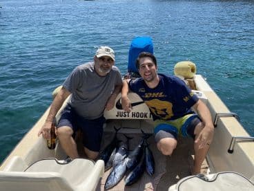 Two anglers enjoying their successful fishing trip, displaying several caught fish on a small boat in clear blue waters.