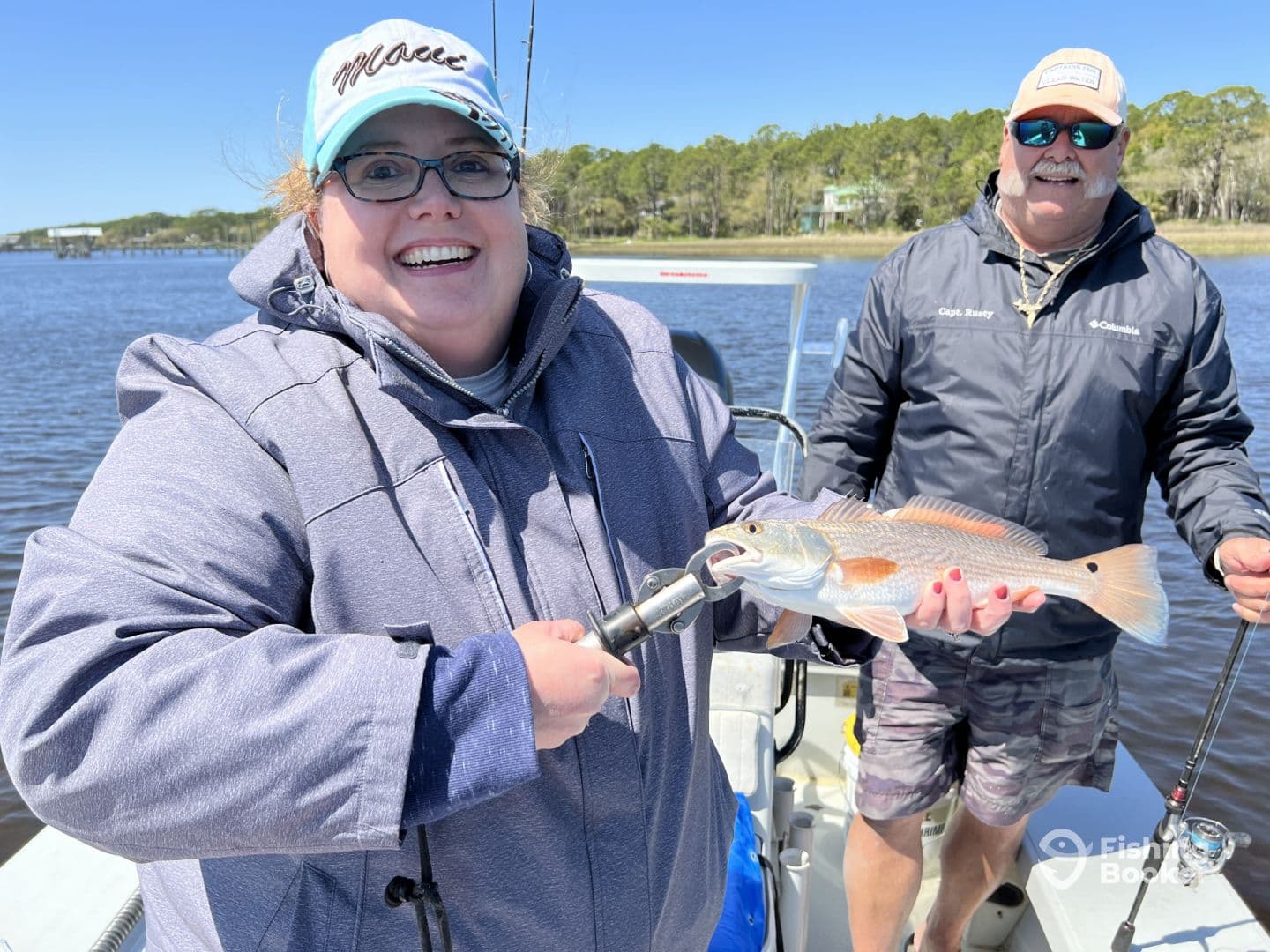 An enthusiastic angler proudly displaying a Redfish while fishing on a sunny day in a scenic coastal environment.