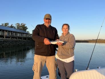 Two anglers proudly displaying their catch, a Speckled Trout, while enjoying a serene fishing trip on the water.