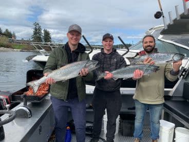Three anglers proudly displaying their catch of Chinook Salmon on a fishing charter in a scenic coastal environment.
