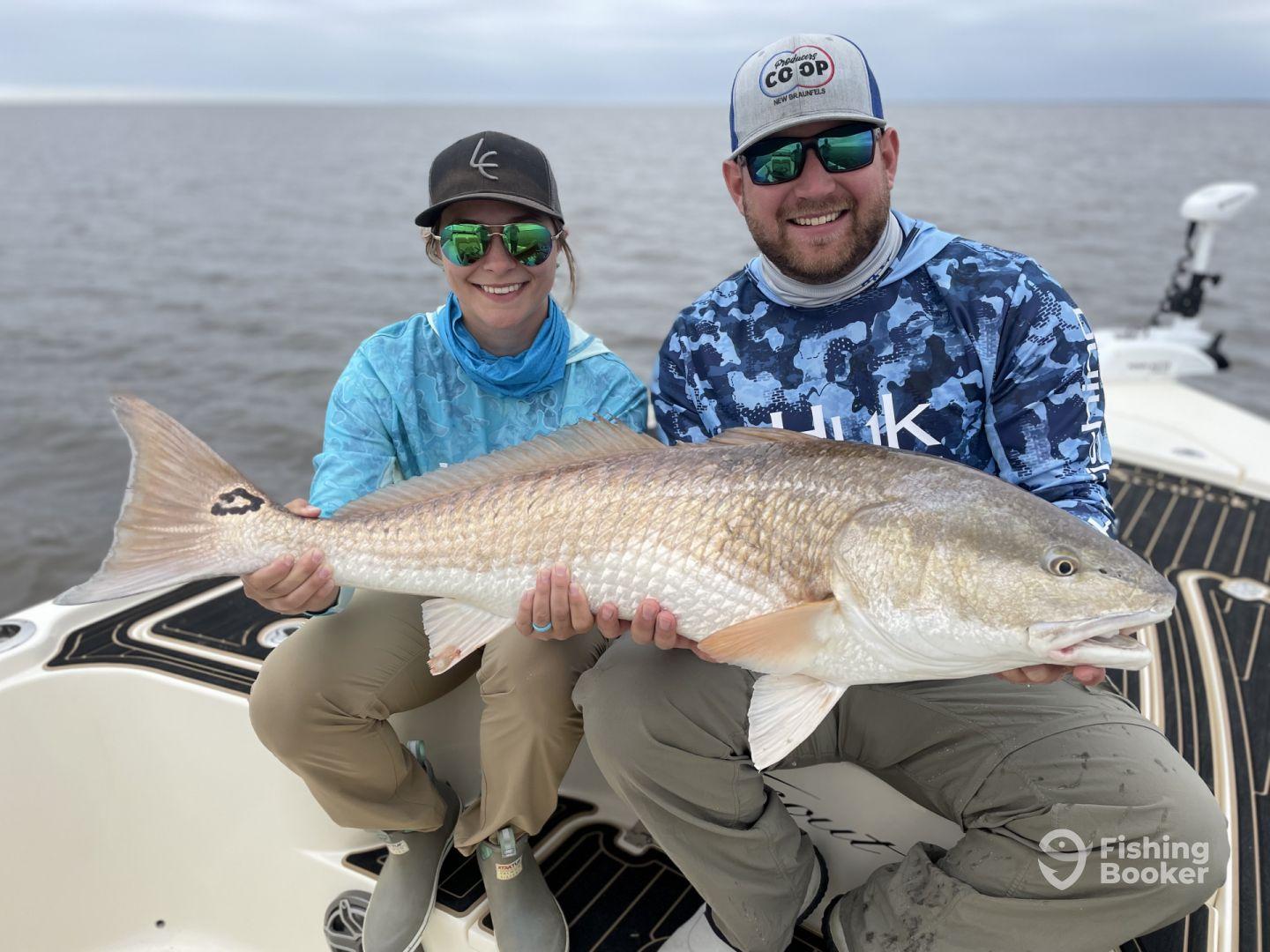 Two anglers proudly displaying a large Redfish while fishing from a boat in a coastal environment.
