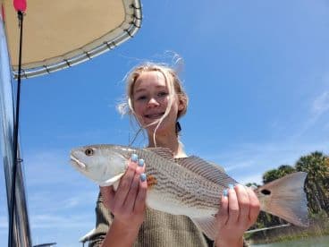 A young angler proudly displaying a Redfish while fishing on a sunny day, showcasing the excitement of youth fishing adventures.