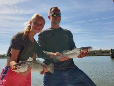 A young angler and an adult proudly displaying their catches of Speckled Trout while enjoying a day on the water.
