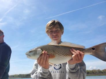 Young angler proudly displaying a Redfish while fishing on a sunny day in Florida.