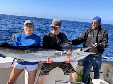 Three anglers proudly displaying a large Swordfish while out on the open ocean, showcasing a successful deep-sea fishing trip.