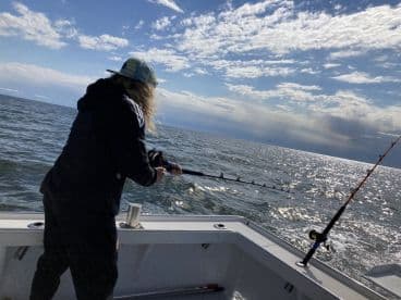 An angler casting a line into the sparkling waters while fishing from a boat, showcasing a beautiful day on the ocean.