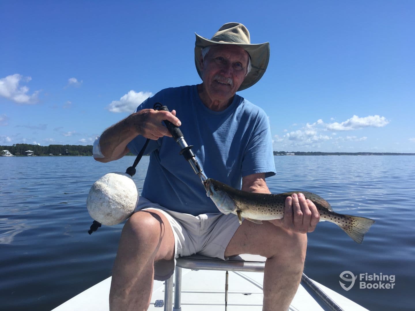 An older angler proudly displaying a Speckled Trout while fishing on a calm lake, showcasing a beautiful day on the water.