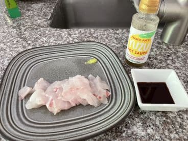 Freshly sliced fish fillets displayed on a plate, accompanied by Yuzu hot sauce and soy sauce, ready for a delicious meal.