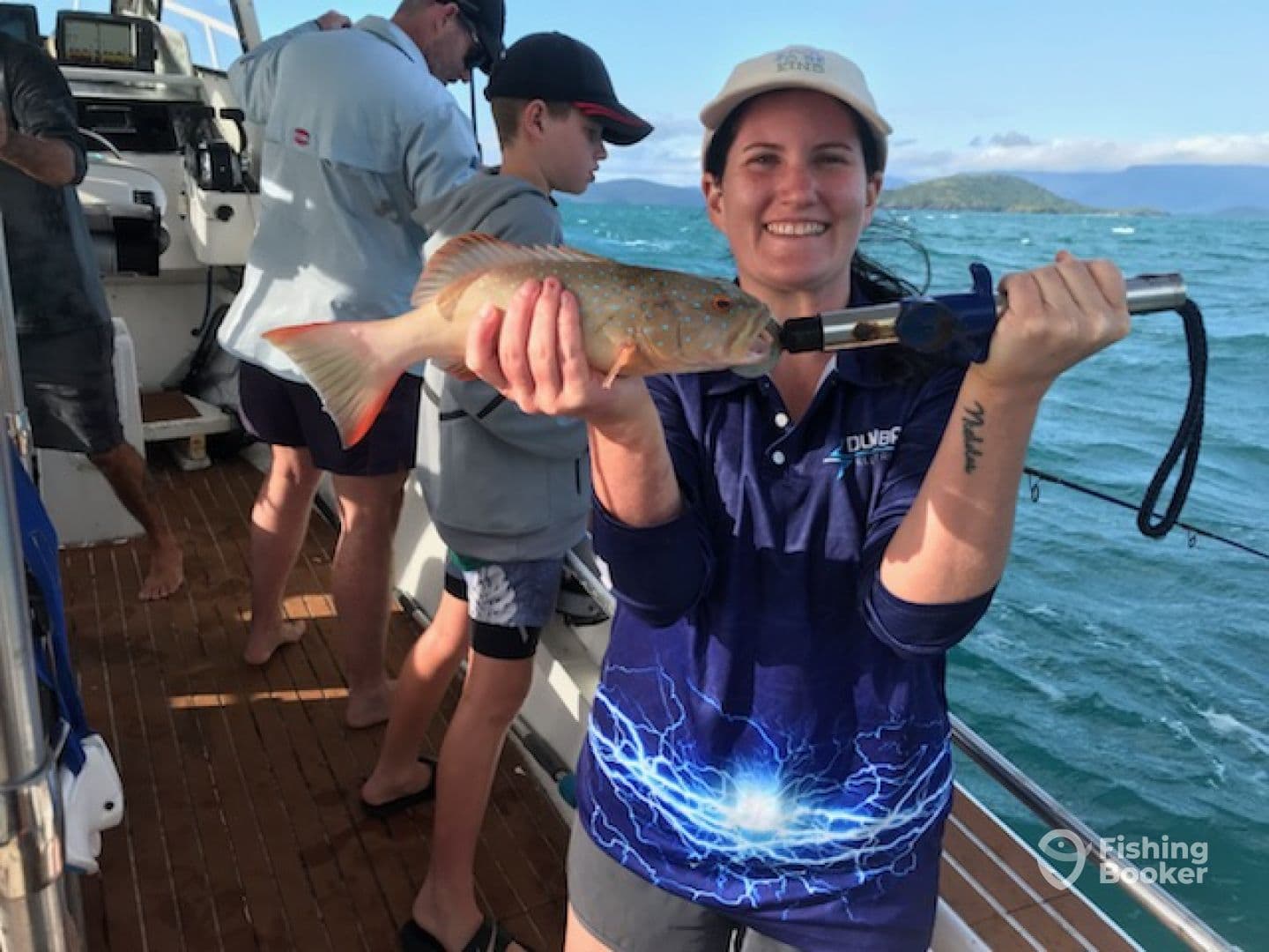 A woman proudly displays her catch, a colorful fish, while fishing with family on a boat in a scenic coastal environment.