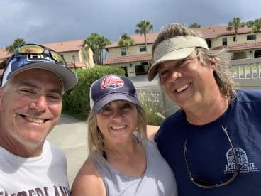Three individuals smiling for a selfie, likely after a fishing trip, with a residential backdrop.