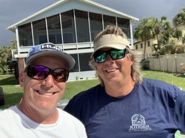 Two smiling individuals posing for a selfie in front of a house, with no fishing activity or catch visible.