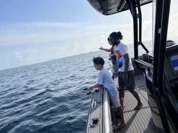 A young angler and an adult are actively fishing from a sleek boat, enjoying a day on the water with a clear blue sky in the background.