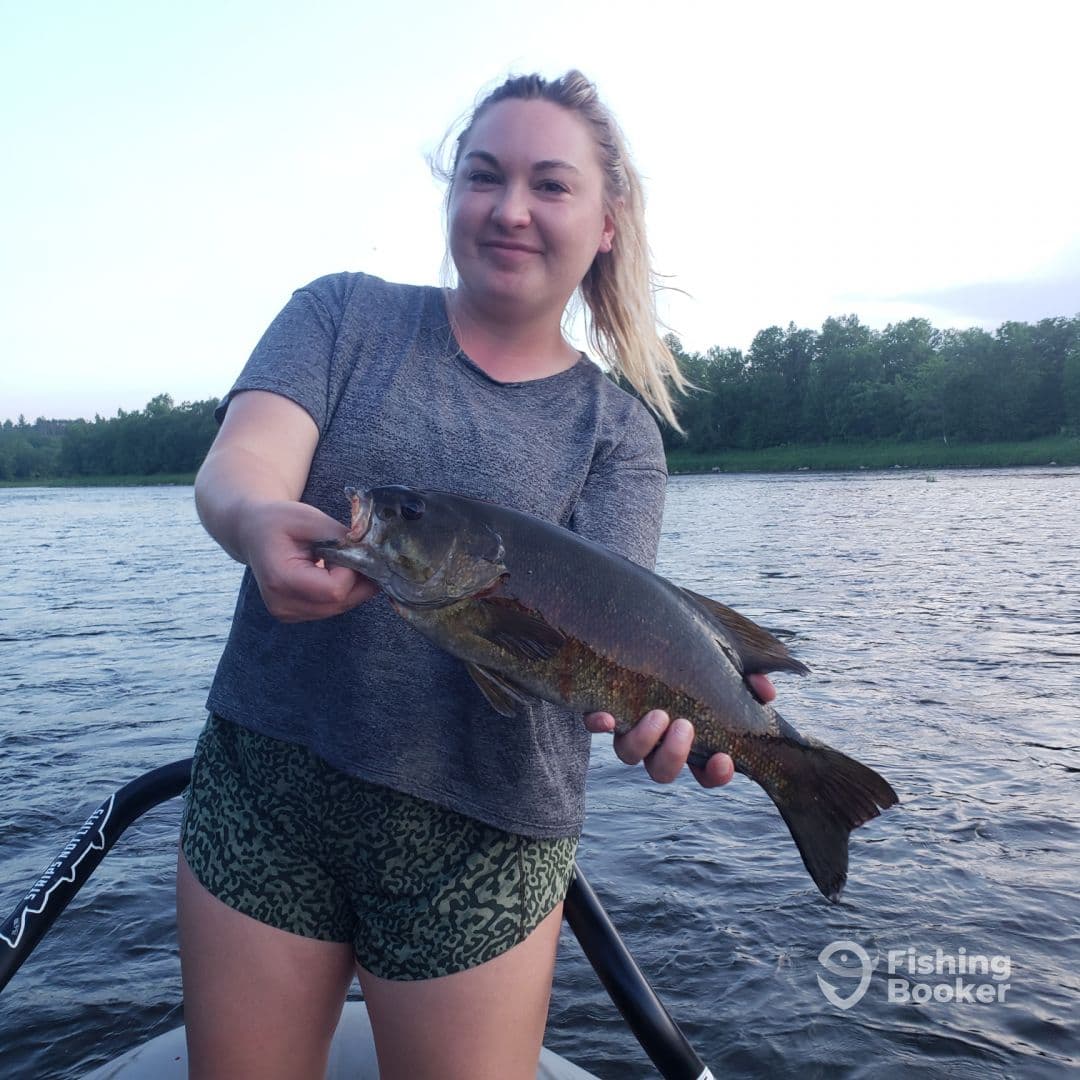 An angler proudly displaying a large Largemouth Bass while fishing on a serene lake.