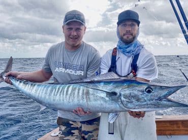 Two anglers proudly displaying a large Wahoo while fishing offshore, showcasing the thrill of deep-sea fishing.