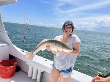 A smiling angler proudly displays a large Redfish while fishing on a sunny day in open waters.