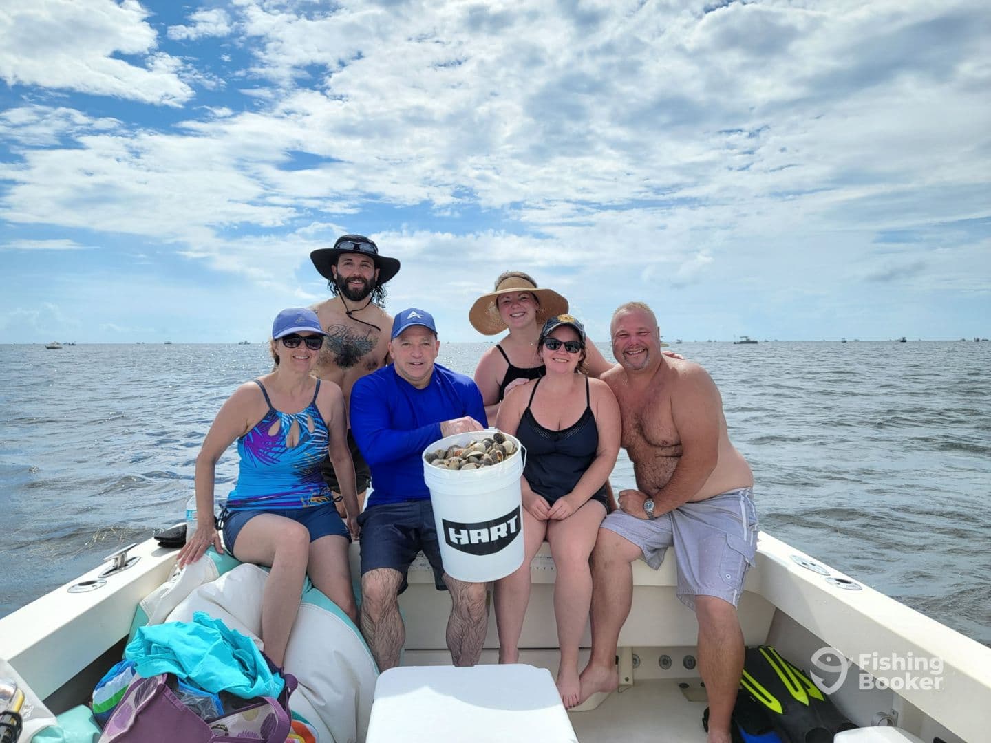 Group of six enjoying a day on the water, holding a bucket, likely filled with clams or shellfish, while relaxing on a boat.
