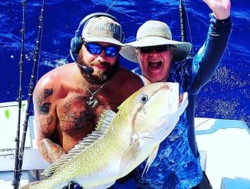 Two anglers celebrating a successful catch of a large Yellowtail Snapper while out on the open ocean.