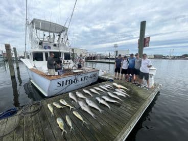 A group of anglers posing with their catch of various fish, including Mahi Mahi and Snapper, displayed neatly on the dock next to the 'Shine Eye Girl' charter boat in Nags Head, NC.