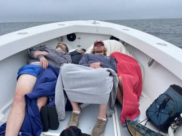 Group of anglers resting on the boat during a cloudy day at sea, showcasing a relaxed fishing trip atmosphere.