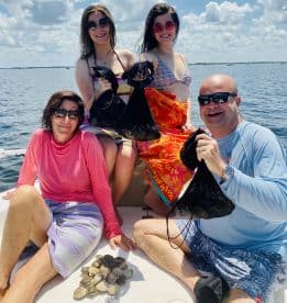 A family enjoying a day on the water, proudly displaying their catch of scallops while relaxing on a boat.