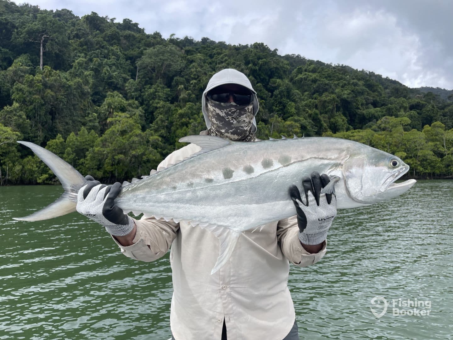 Angler holding a large Trevally while fishing in a lush tropical environment.
