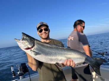Angler proudly displaying a large Salmon while fishing on a boat in open waters.