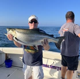 Angler proudly displaying a large Salmon while fishing on a boat in open waters.