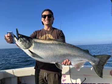 Angler proudly displaying a large Salmon while fishing on a boat in open waters.