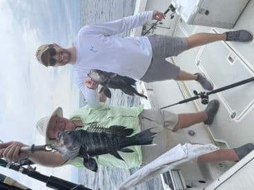 Two anglers proudly displaying their catch of Black Drum while fishing on a charter boat.